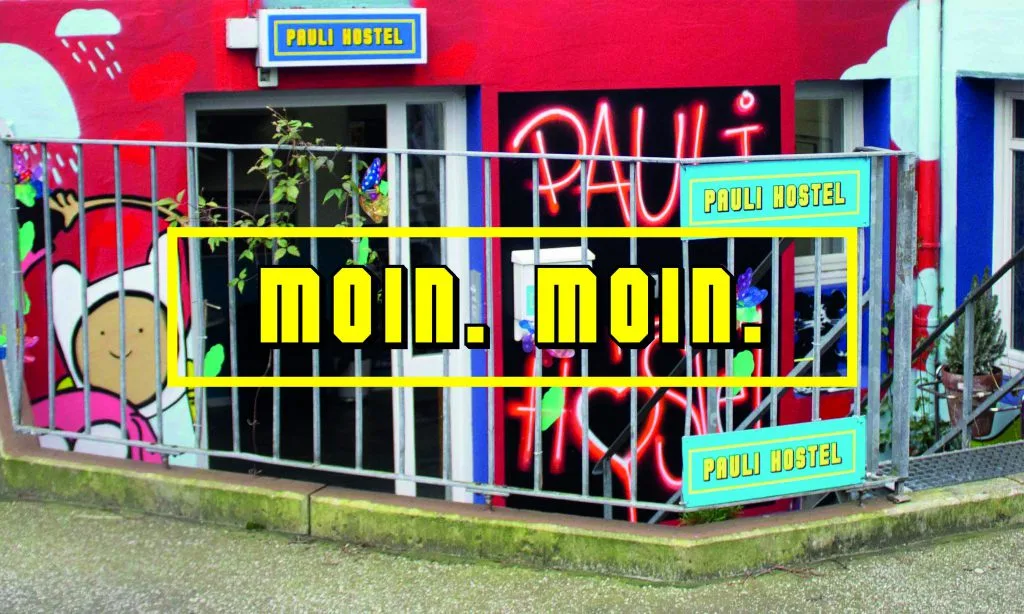 Colorful street art facade of Pauli Hostel in Hamburg, featuring vibrant murals and neon graffiti with a 'Moin Moin' greeting overlay.