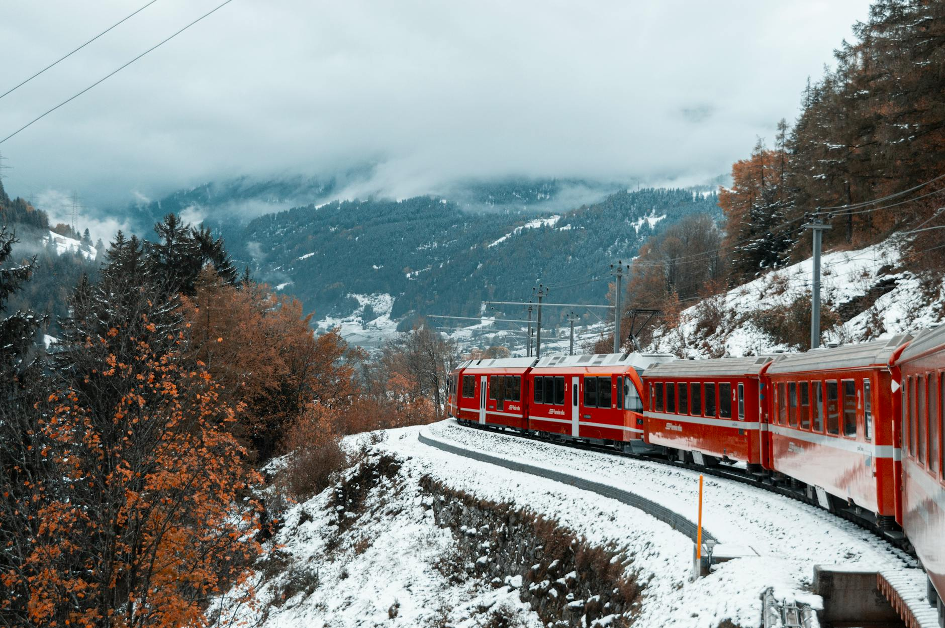 Ein Schweizer Panoramazug fährt durch eine malerische Berglandschaft mit schneebedeckten Gipfeln und grünen Wiesen, symbolisiert die bequeme und nachhaltige Reiseerfahrung mit dem Swiss Travel Pass.