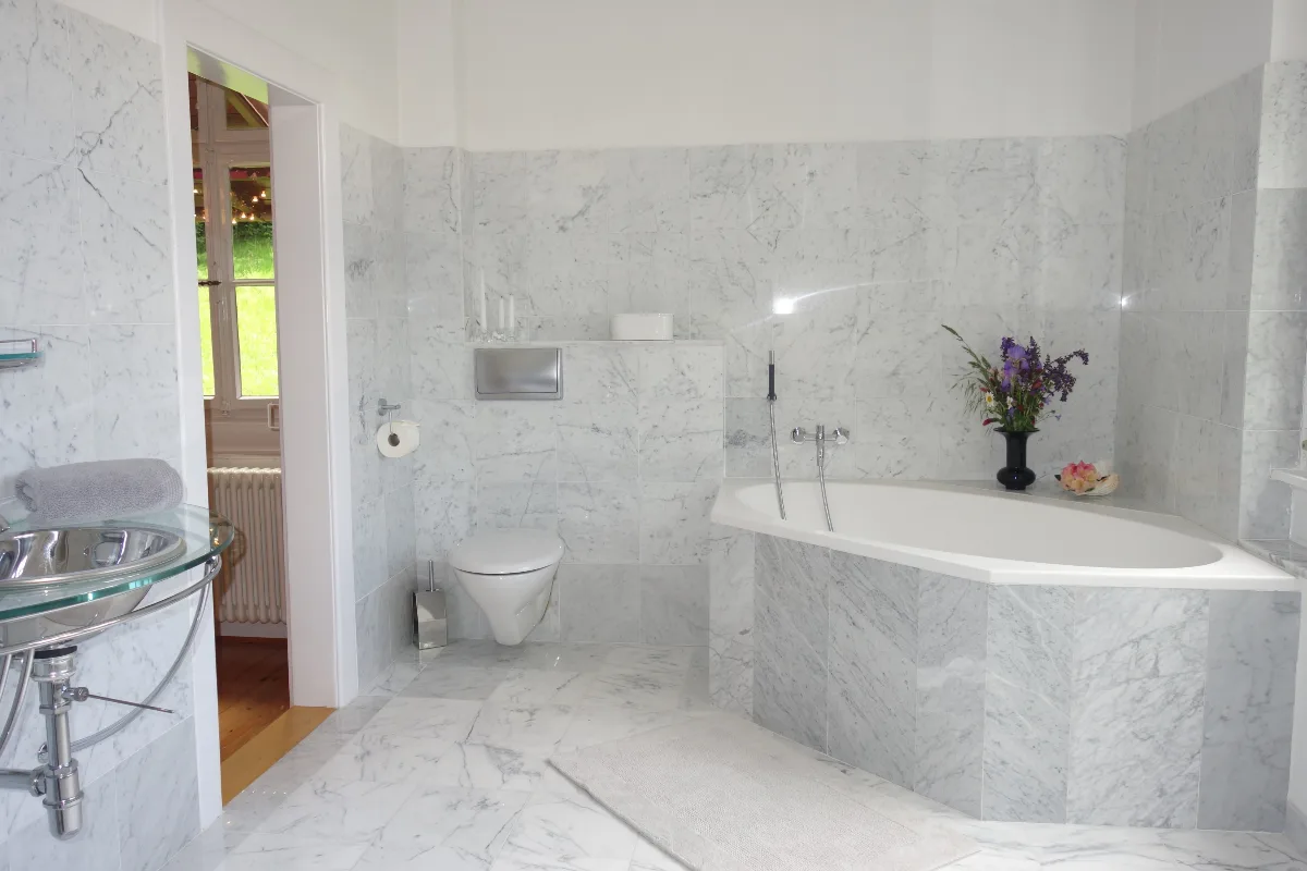 Elegant marble bathroom with corner bathtub, wall-hung toilet, and glass washbasin.