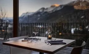 Elegantly set dining table for two with glassware and candle overlooking mountain twilight.