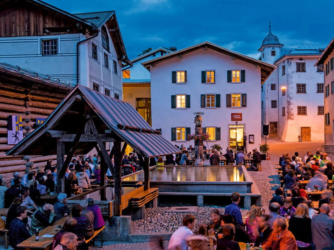 Ein idyllisches Bergdorf in Graubünden mit traditionellen Walserhäusern, umgeben von grünen Wiesen und Bergen, das für nachhaltigen Tourismus ausgezeichnet wurde.