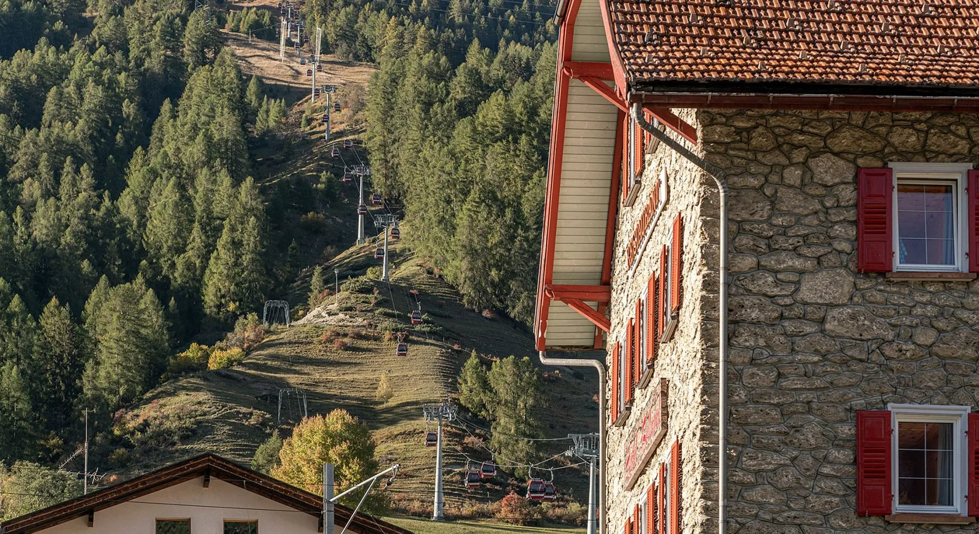 The historic stone facade of Hotel Bellaval with red shutters perfectly establishes the century-old Alpine hotel at the heart of Scuol.