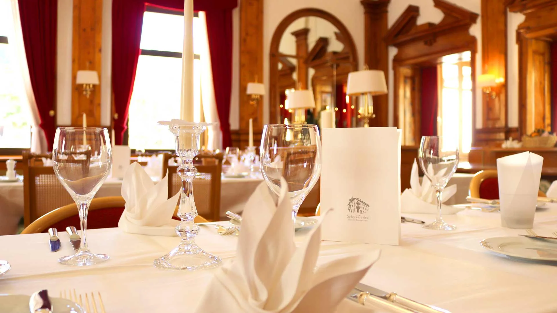 Elegantly set dining room with white linens, crystal glasses, candles, and rich wood panelling.