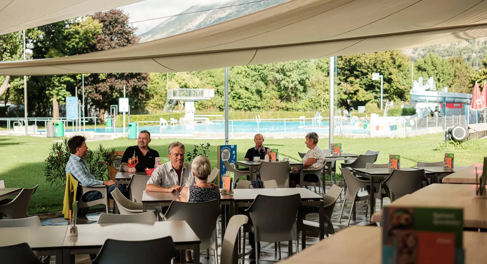 Guests relaxing and socializing at the shaded outdoor restaurant terrace overlooking the swimming pool.