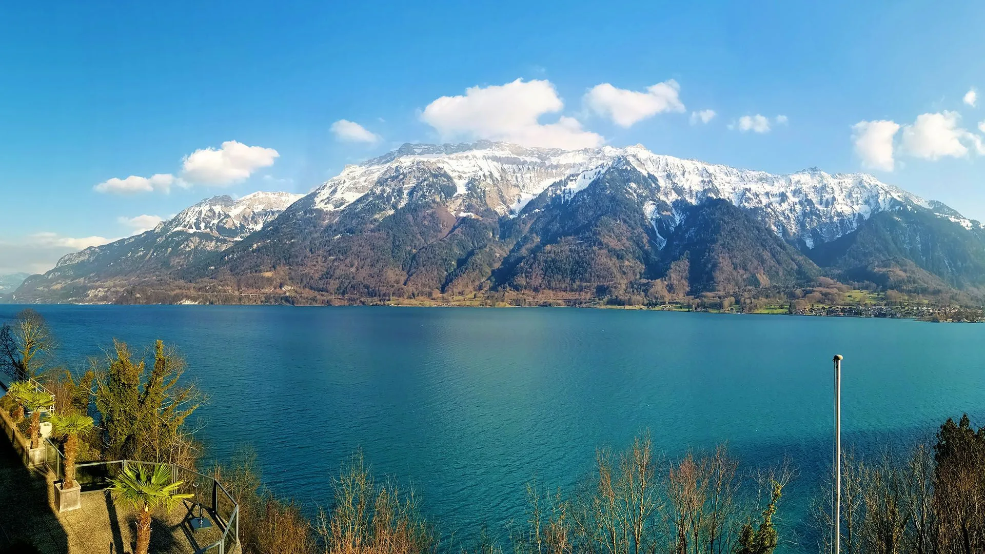 Panoramic view of turquoise Lake Brienz with snow-capped mountains under a clear blue sky.