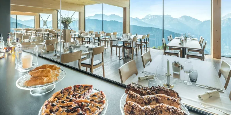 Aerial view of Hotel Belalp nestled in alpine meadow with Aletsch Glacier and UNESCO peaks visible—iconic establishment shot.