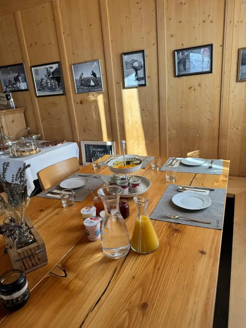 Cozy wooden dining room set for breakfast with juice, jams, and fresh fruit, showcasing the welcoming atmosphere of the Ustreia Orta.