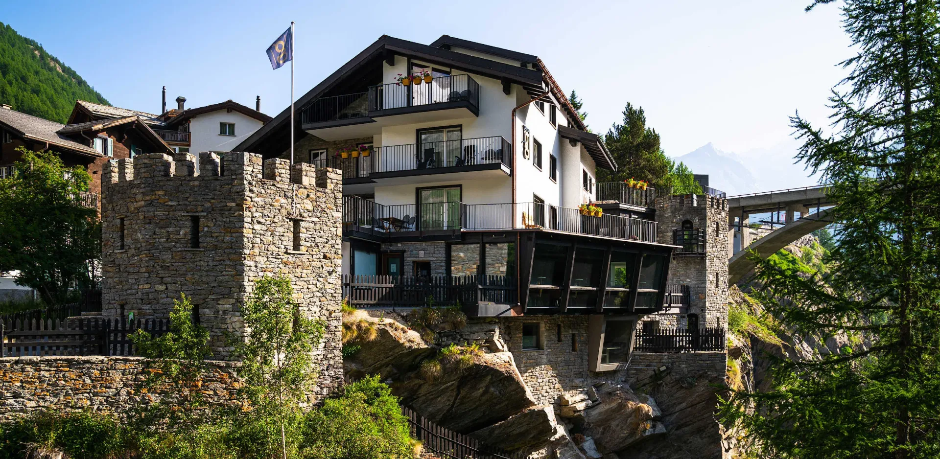 Dramatic exterior of Hotel La Gorge perched on ancient stone castle walls above rocky cliffs, perfectly capturing the unique alpine character of this Saas-Fee boutique hotel.