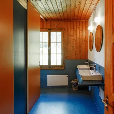 A colourful, freshly renovated bathroom with warm wood panelling, blue floors and orange accents.
