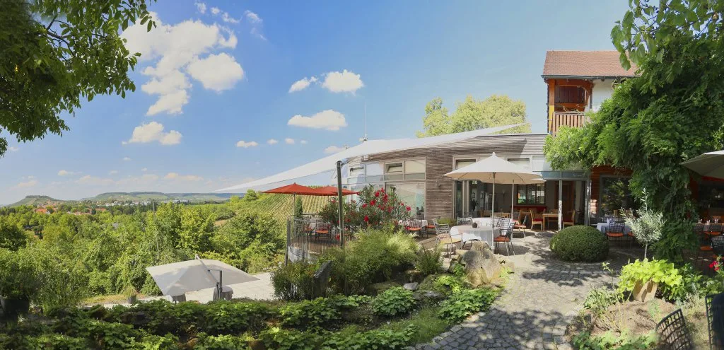 Sunlit terrace of the Rappenhof hotel with outdoor dining tables overlooking rolling vineyard landscape.