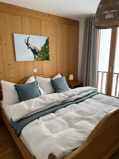 Charming pine-wood bedroom with ibex artwork and balcony, illustrating the cozy, nature-inspired accommodation style of the Ustreia Orta.
