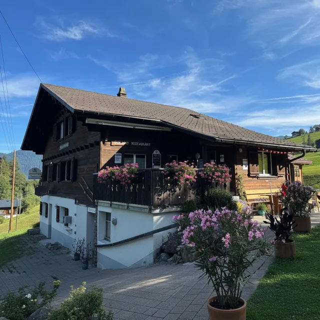 A smiling man takes a selfie inside the cozy wooden restaurant with a stunning mountain chapel view behind him.
