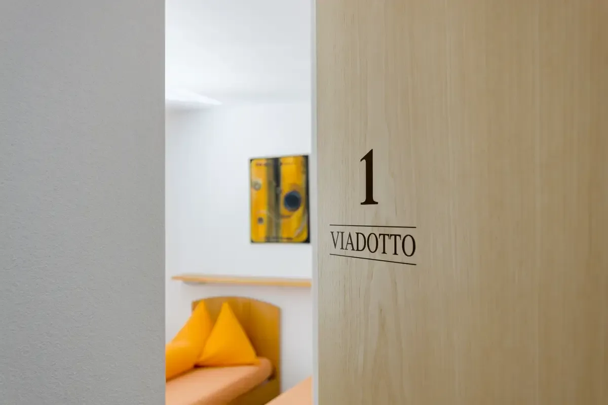 Wooden door panel labeled '1 Viadotto' opens to reveal a bright, orange-accented room beyond.