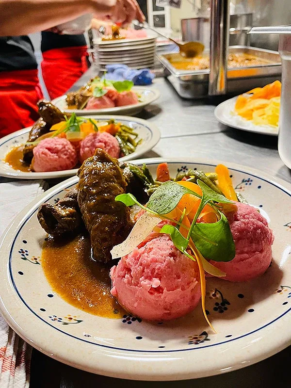 Plated main course with dark meat roll, pink dumplings, glazed vegetables and fresh herbs.