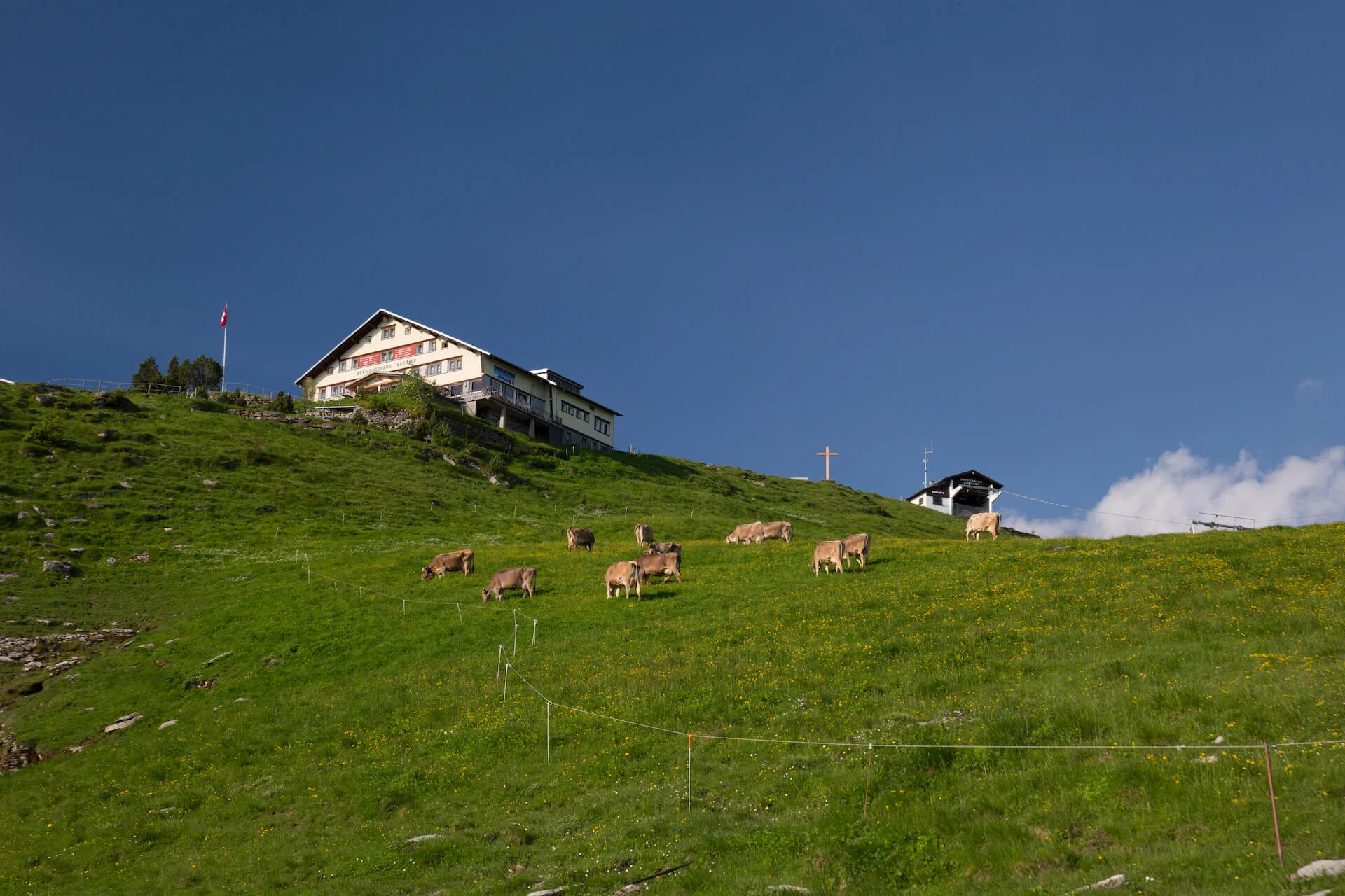 The Berggasthaus Ebenalp mountain inn glows in warm golden sunset light atop dramatic limestone cliffs.