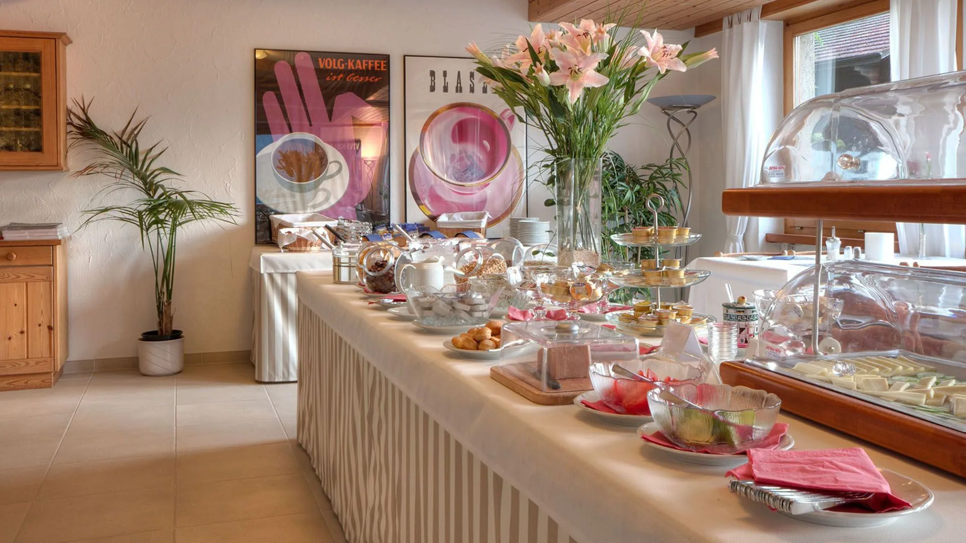 Generous breakfast buffet spread with pastries, cheeses, and fresh flowers in a warmly lit dining room.