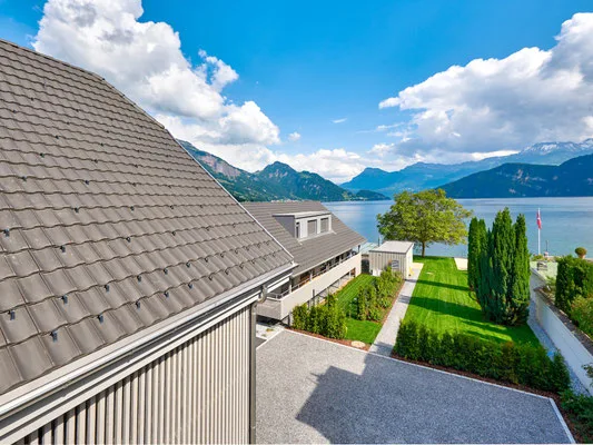 Aerial view of Villa Pescheria's roof and lush garden leading down to the lake and mountains.