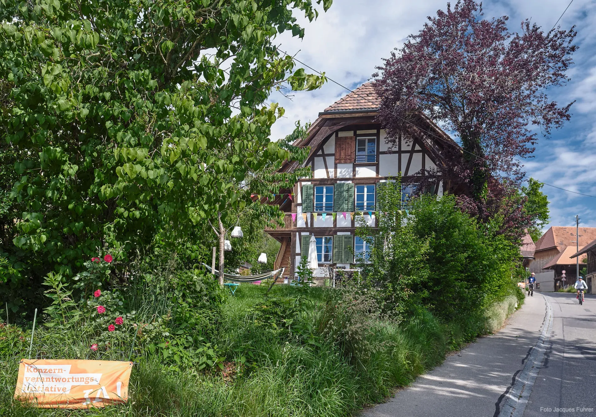 Charming half-timbered farmhouse exterior with green shutters, colorful bunting, and lush garden—the restored Stöckli welcoming guests.