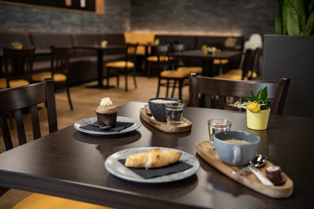 Cozy café interior with dark wood tables set with coffee, croissant, and chocolate cupcake.