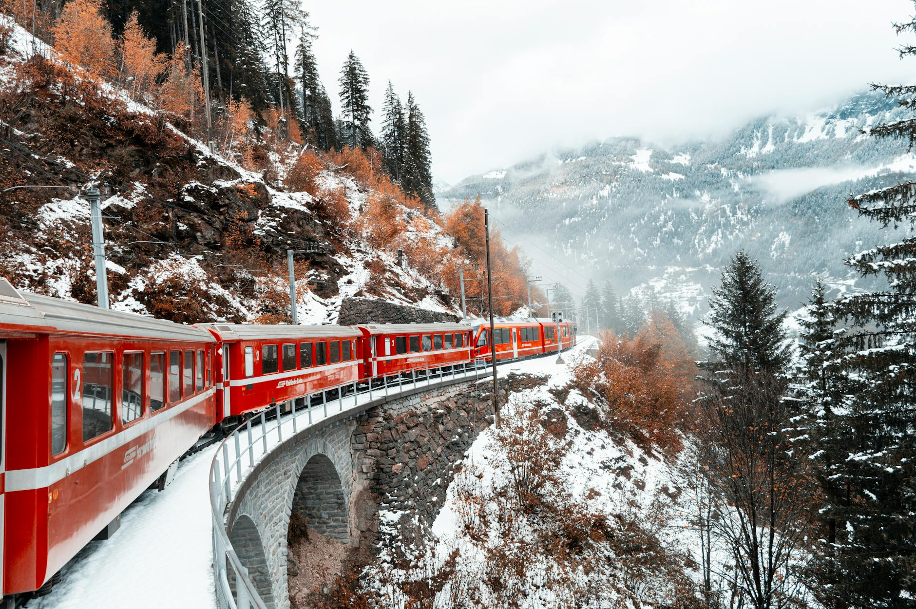 Ein Schweizer Panoramazug fährt durch eine malerische Berglandschaft mit schneebedeckten Gipfeln und grünen Wiesen, symbolisiert die bequeme und nachhaltige Reiseerfahrung mit dem Swiss Travel Pass.